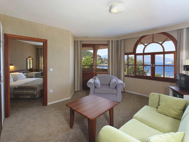 Kleines Wohnzimmer mit grünem Sofa, zwei Sesseln, Holztisch und Fenster mit Blick ins Grüne.