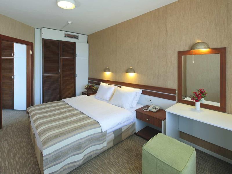 Helles Hotelzimmer mit Doppelbett, braunen Wänden, Spiegel, Tisch, Hocker und zwei Lampen.