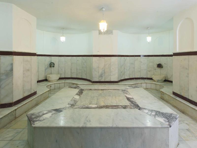 Innenraum eines Hamams mit weißem Marmor, traditionellem Waschbecken und warmem Deckenlicht.