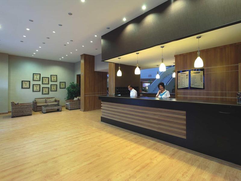 Moderne, helle Hotelrezeption mit Holzfußboden, Empfangstresen und Wartebereich mit Sesseln.