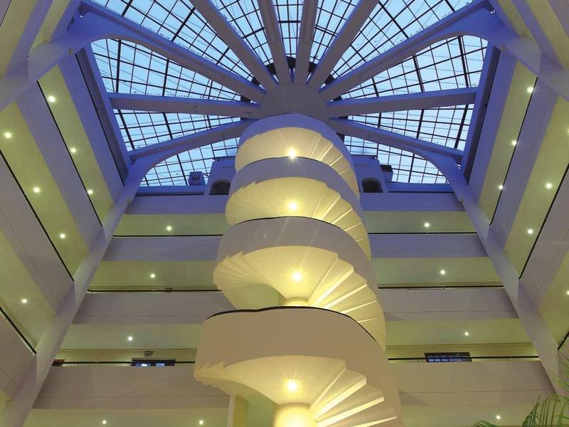 Ein runder, weißer Treppenaufgang mit einem Glaskuppeldach und mehreren Stockwerken.