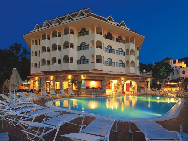 Großes Hotel mit beleuchtetem Außenpool, Liegestühlen und mehrstöckiger Fassade bei Abenddämmerung.