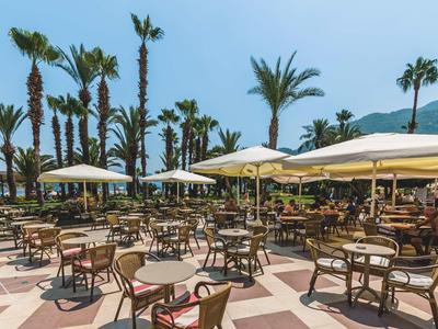 Duży taras z stołami, krzesłami i parasolami obok palm i gór.