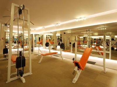 Helles Fitnessstudio mit verschiedenen Trainingsgeräten und Spiegeln an den Wänden.