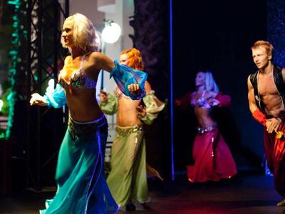 Tänzer in bunten Kostümen führen eine Show auf einer Bühne mit dunklem Hintergrund auf.