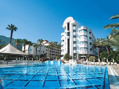 Duży basen hotelowy z fontannami, otoczony leżakami i palmami w słoneczną pogodę.