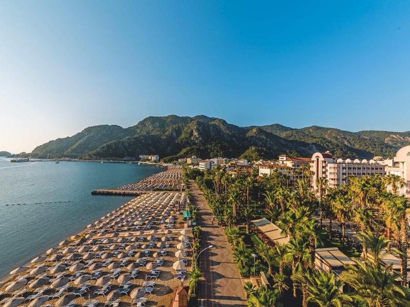 Plaża z parasolami i palmami wzdłuż wybrzeża z górami i budynkami hotelowymi.