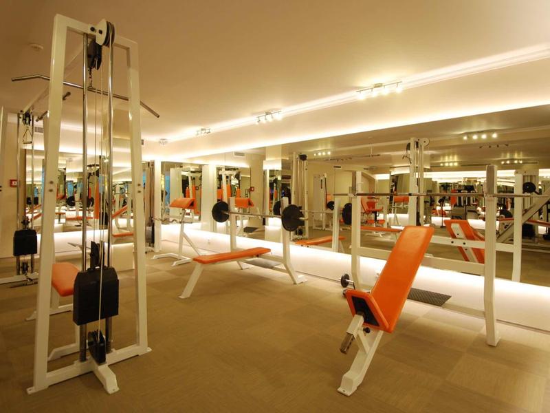 Nowoczesna siłownia z wielofunkcyjnymi maszynami do ćwiczeń i pomarańczowymi siedzeniami.