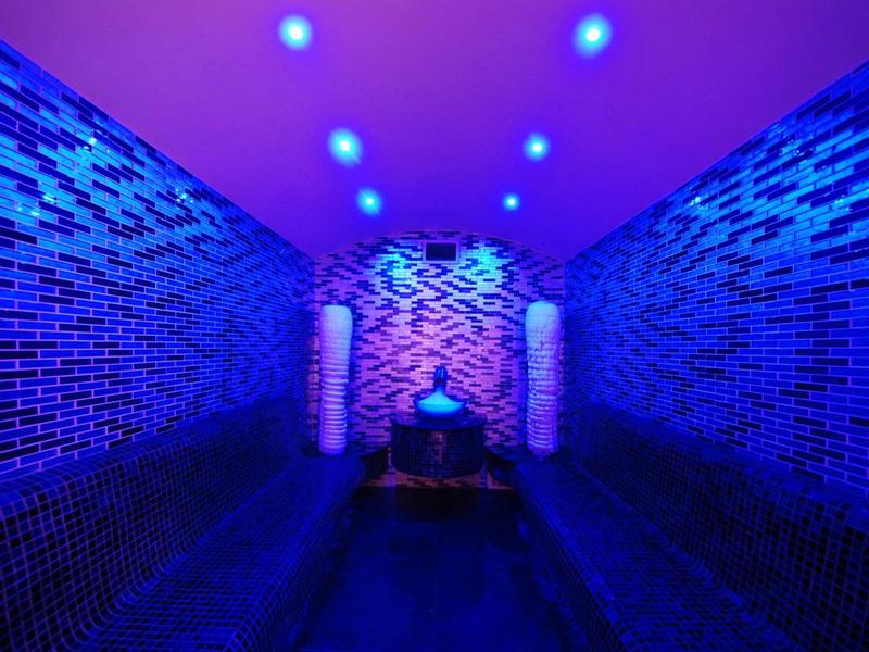 Wąska relaksująca sauna z niebieskimi światłami LED i dekoracyjnymi ścianami z małych płytek.