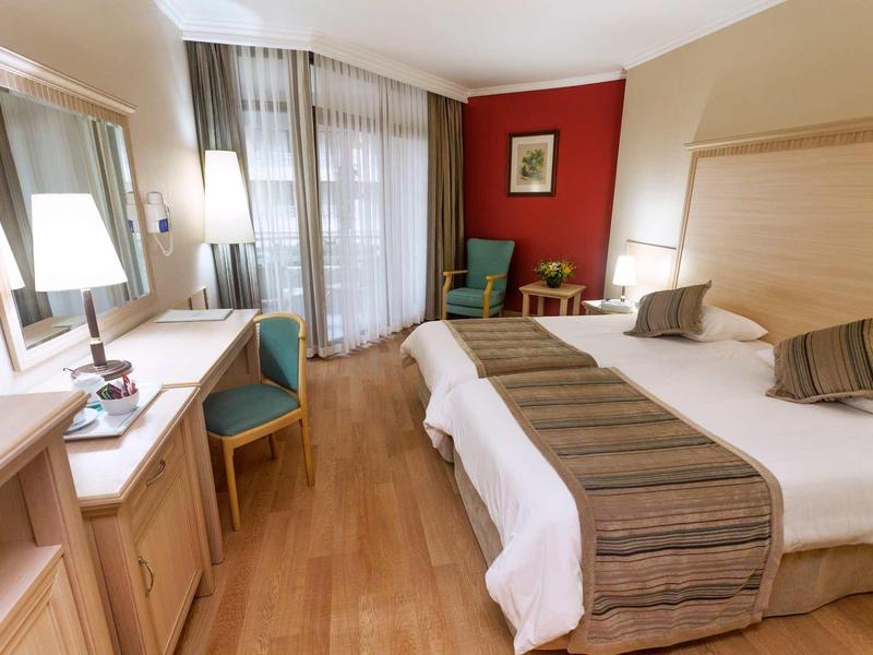 Przytulny pokój hotelowy z dwoma pojedynczymi łóżkami, biurkiem, fotelami i drewnianą podłogą.