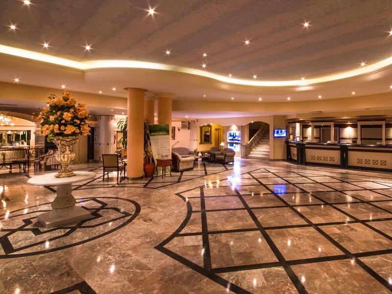 Przestronny hol hotelowy z błyszczącą marmurową podłogą i eleganckim oświetleniem sufitowym.