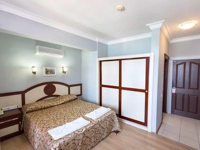 Helles Hotelzimmer mit Doppelbett, Garderobe und Nachttischen in gedeckten Farben.