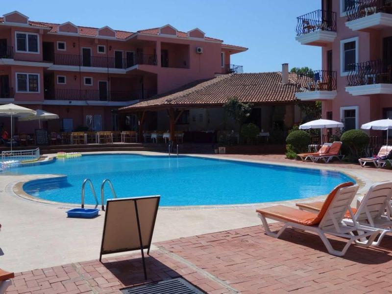 Ein rechteckiger Pool mit blauen Fliesen umgeben von Liegestühlen und zwei mehrstöckigen Gebäuden.