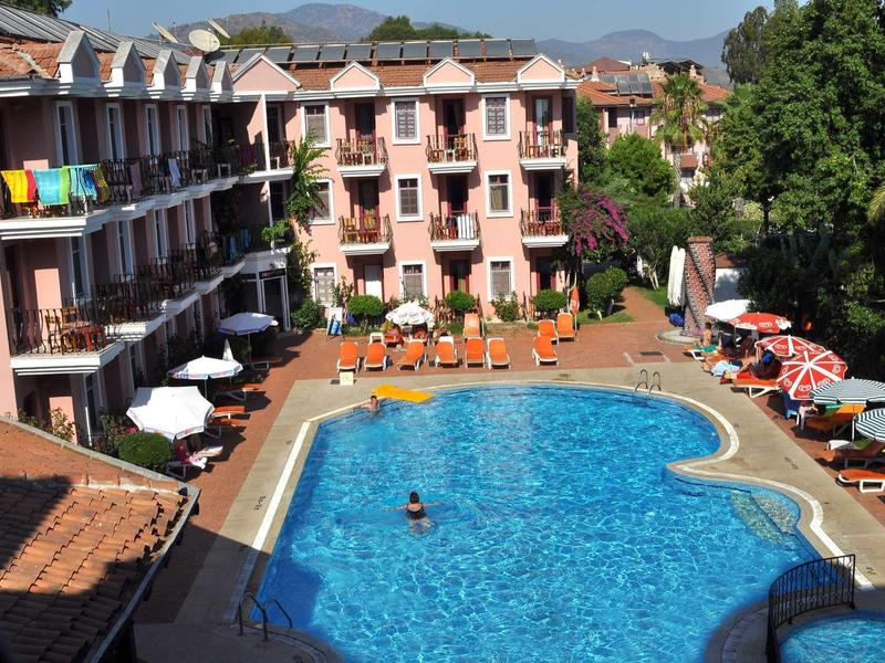 Ein großer blauer Pool umgeben von Liegestühlen, Sonnenschirmen und einem dreistöckigen Hotel.