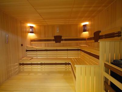 Helle Holzbänke und Wände in einer rechteckigen Sauna mit zwei Wandlampen.