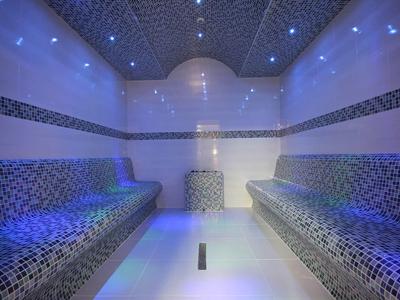 Innenraum einer Sauna mit blauen Mosaikfliesen und indirekter LED-Beleuchtung an Decke und Sitzen.