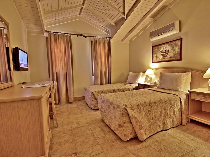 Kleines Schlafzimmer mit zwei Einzelbetten, braunen Vorhängen, Holzmöbeln und warmem Licht.