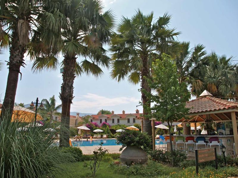 Hotelgarten mit Palmen, Schwimmbecken, Liegestühlen und Sonnenschirmen bei klarem Himmel.