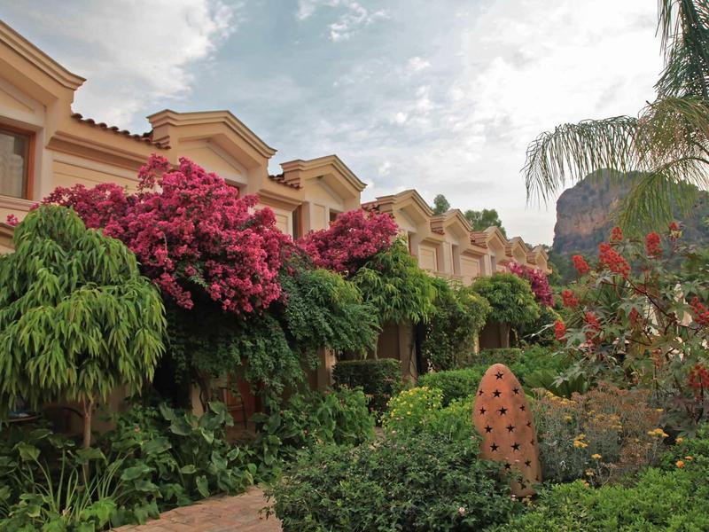 Reihenhäuser mit blühenden roten Bougainvillea und grünen Gärten unter bewölktem Himmel.