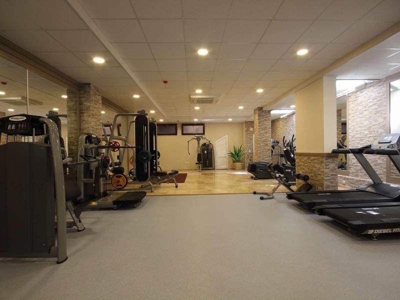 Moderner Fitnessraum mit Laufbändern, Kraftgeräten und Hantelbereich, helle Beleuchtung, saubere Atmosphäre.