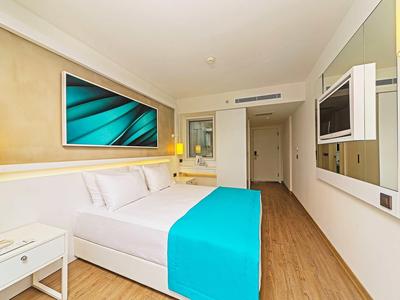 Modernes Hotelzimmer mit weißem Bett und türkisfarbenen Akzenten, Holzboden und großem Wandbild.