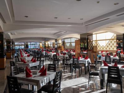 Großer, heller Speisesaal mit vielen Tischen, schwarzen Stühlen und roten Servietten.