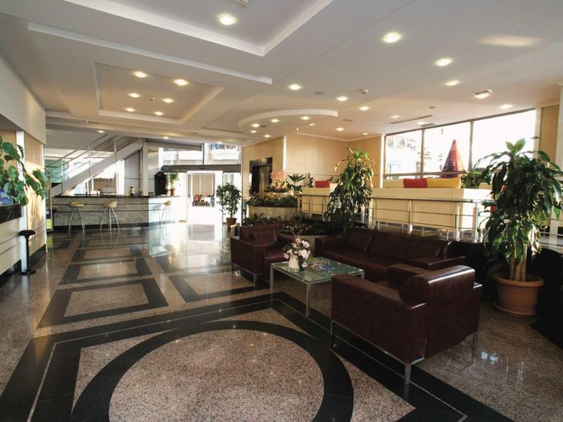 Bright hotel lobby with leather sofas, plants, and large windows.