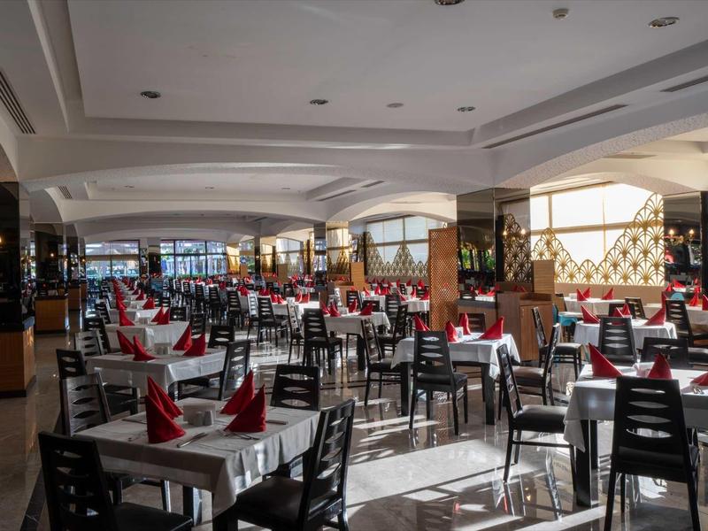 Large brightly lit dining hall with many tables and chairs, decorated with red napkins.