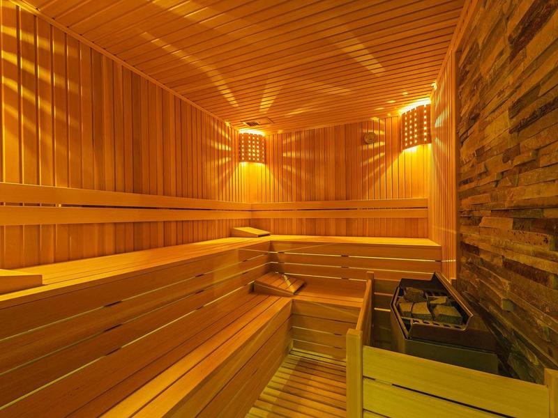 Wooden sauna with warm lighting, benches, and a sauna heater in a cozy room.