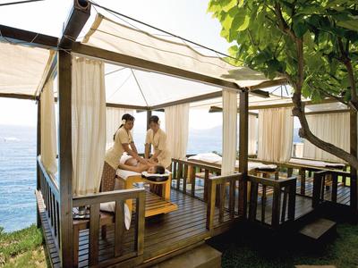 Zwei Personen entspannen in einem offenen Pavillon mit Meerblick und Holzboden.