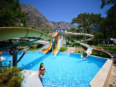 Buntes Wasserrutschenbecken in einem sonnigen Freizeitpark mit Bergen und Bäumen im Hintergrund.