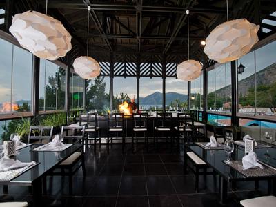 Modernes Restaurant mit großen Fenstern, weißen Lampen, dunklem Boden und Blick aufs Meer.