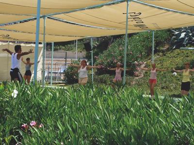 Gruppe von Menschen, die unter einem Sonnenschutz im Freien trainieren, umgeben von Grün.