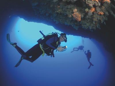 Taucher erkunden eine Unterwasserhöhle im klaren blauen Wasser.