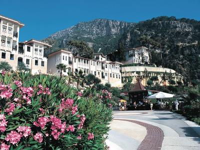 Gebirgslandschaft mit weißem Hotel, blühenden Sträuchern und blauem Himmel im sonnigen Licht.