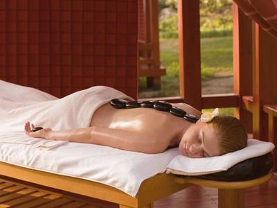 Person liegt auf Massageliege mit heißen Steinen auf dem Rücken in einem Spa-Bereich.