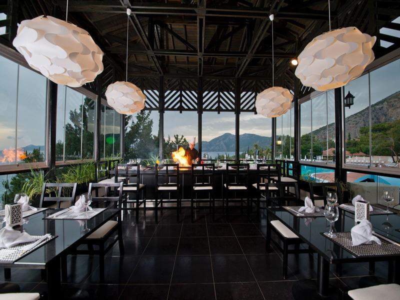Modernes Restaurant mit großen Fenstern, weißen Lampen, dunklem Boden und Blick aufs Meer.
