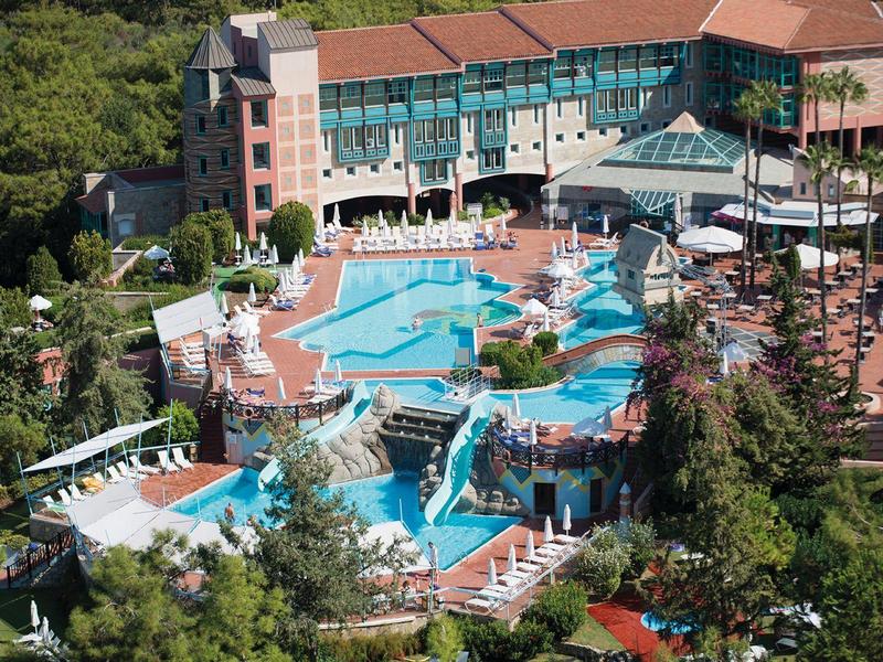 Hotel mit großen blauen Pools, Wasserrutschen, Sonnenschirmen und viel Grün drumherum.