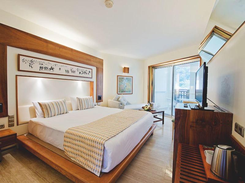 Helles Schlafzimmer mit großem Bett, Holzdekor, großem Fenster und modernem TV an der Wand.