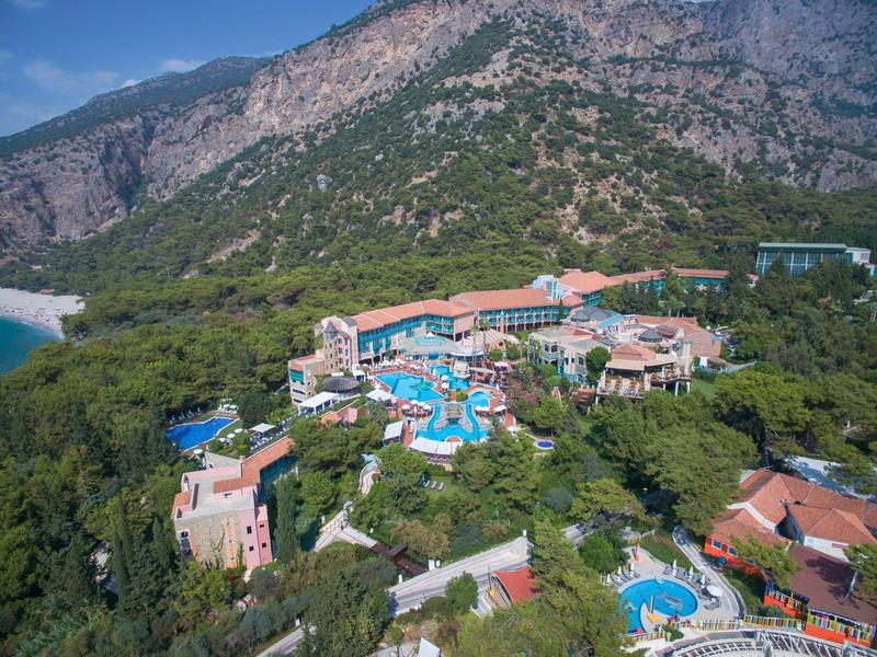 Großes Resort mit mehreren Pools, umgeben von grünen Bäumen und Bergen im Hintergrund.
