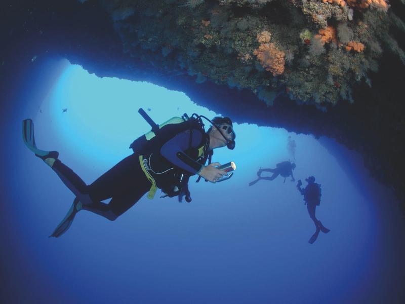 Taucher erkunden eine Unterwasserhöhle, Lichtstrahlen dringen durch das blaue Wasser.