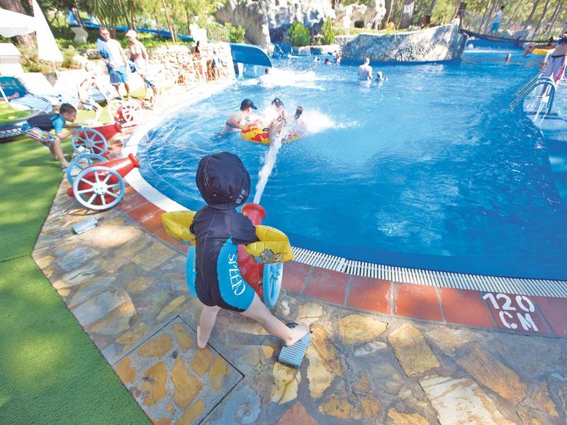 Kinder spielen und schwimmen in einem großen, freien Pool mit klarem blauen Wasser.