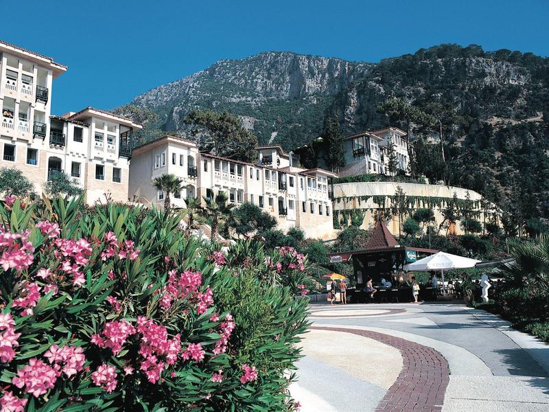 Gebirgslandschaft mit weißem Hotel, blühenden Sträuchern und blauem Himmel im sonnigen Licht.