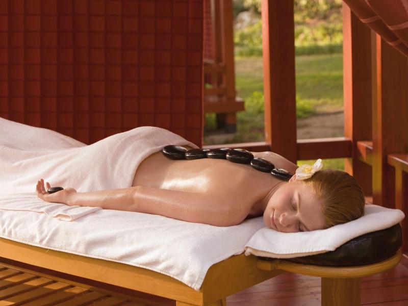 Ein Mann liegt entspannt auf massageliege, mit heißen Steinen auf dem Rücken.