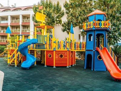 Colorful playground with slides and climbing structures in front of hotel building and trees.