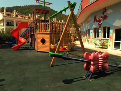 Colorful children's playground with slide, swing, and climbing frame in front of a hotel building.