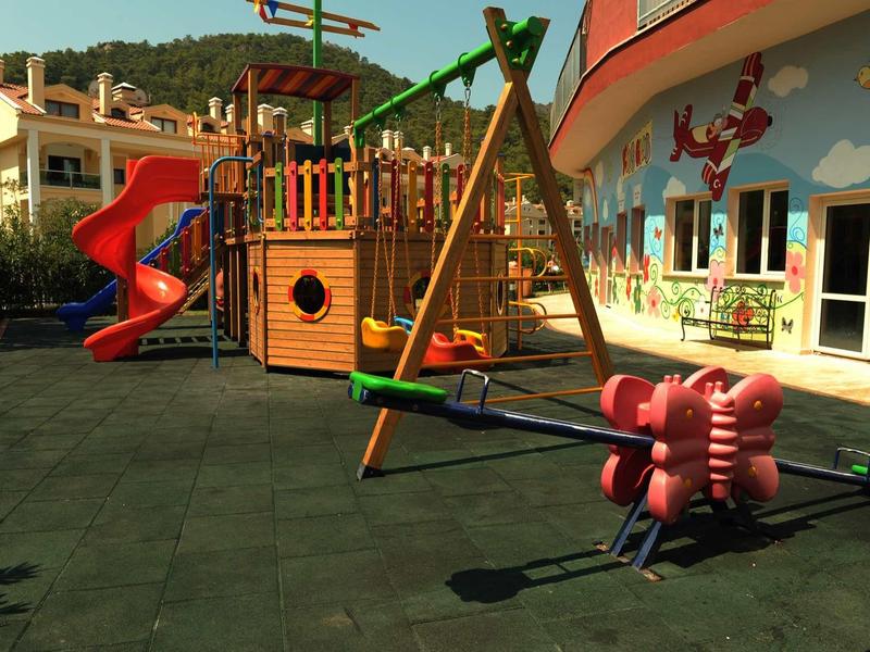 Colorful children's playground with slide, swing, and climbing frame in front of a hotel building.