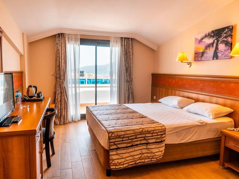 Bright hotel room with double bed, balcony, and TV on wooden floor.
