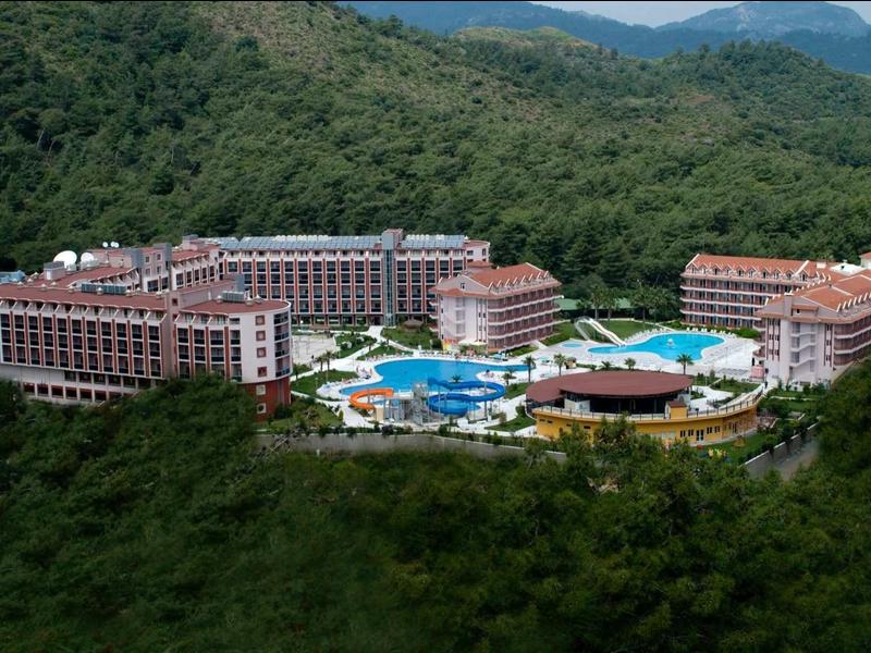 Luxury hotel with multiple buildings and blue pool surrounded by wooded mountains.