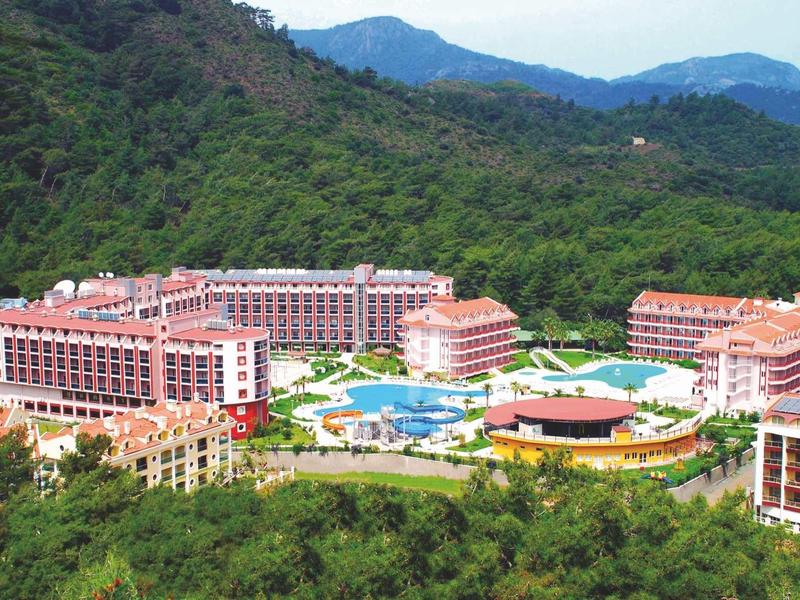 Large resort with multiple buildings and pool surrounded by green mountains.